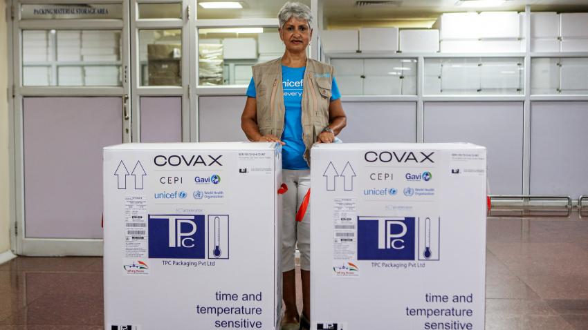 Yasmin is pictured inside a vaccine manufacturing plant. She stands between 2 large COVID vaccine containers.