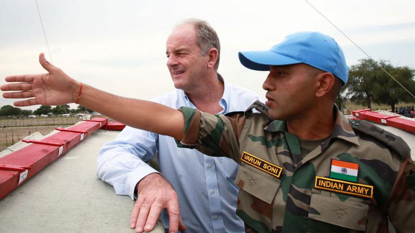 An officer from the Indian army is on a rooftop with David Shearer. The officer is pointing left and both men are looking in that direction.