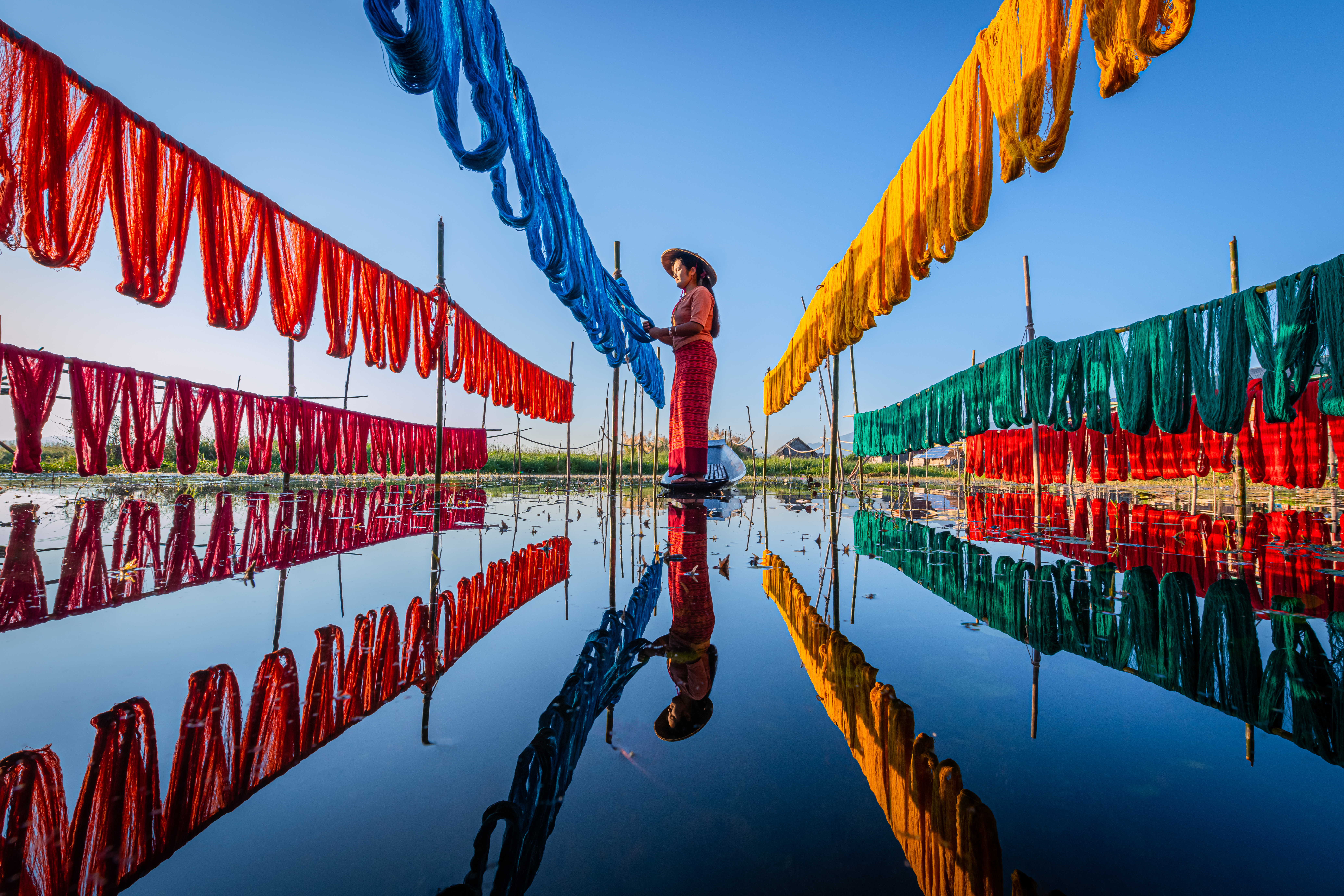 A woman hanging to dry clothes in rows of colourful clothes.