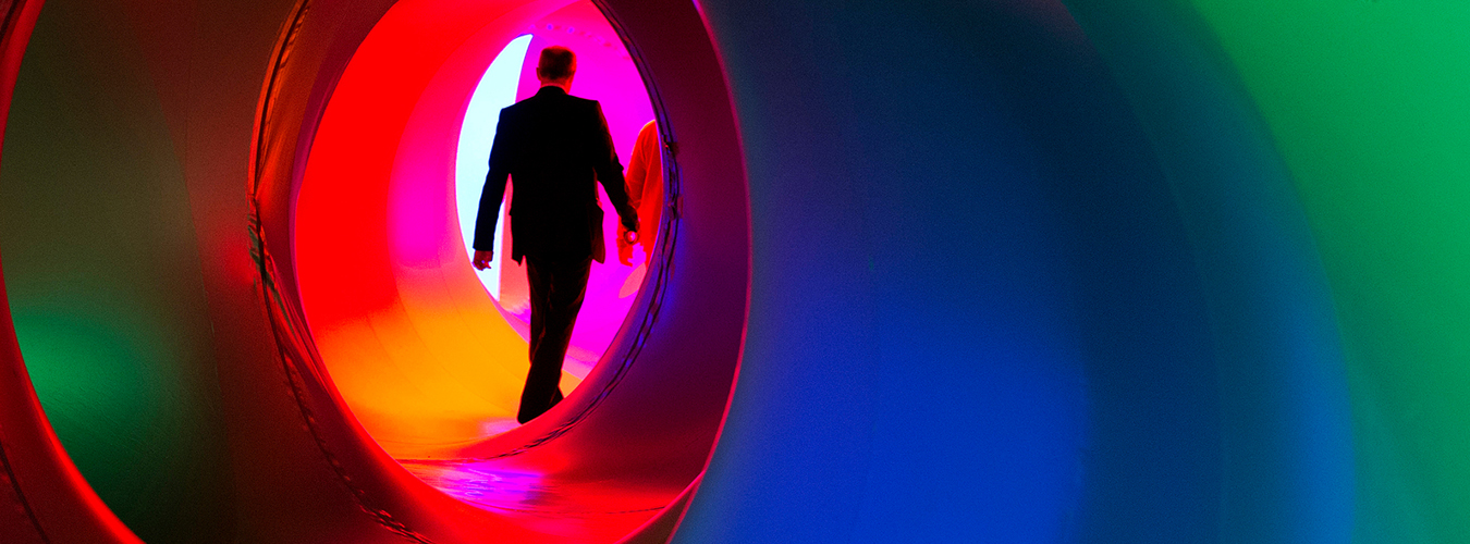 A James Bond style photo of a man walking through a multicolored sculpture that resembles a camera's aperture.