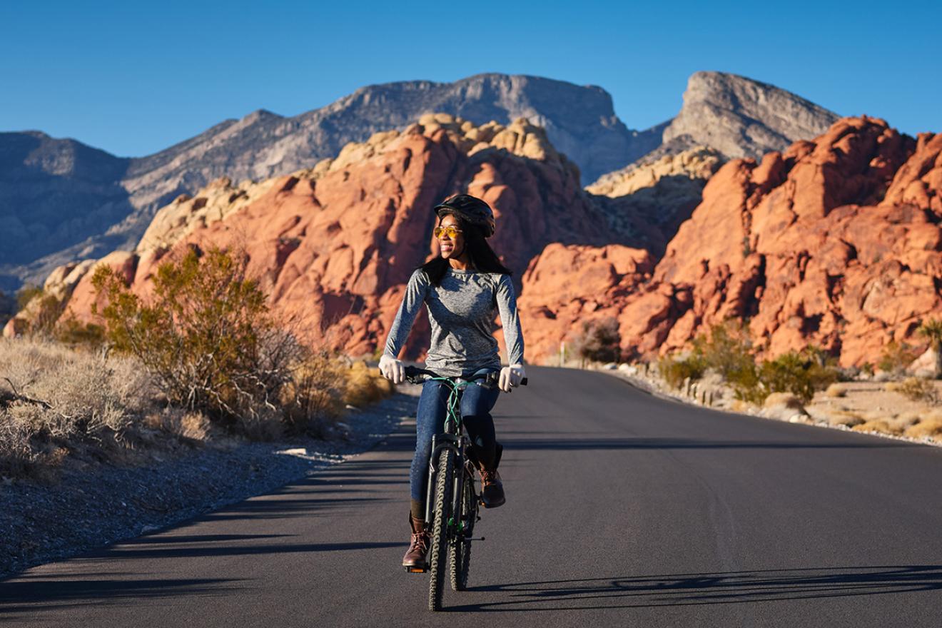 Mujer en bicicleta con un fondo de montañas áridas.