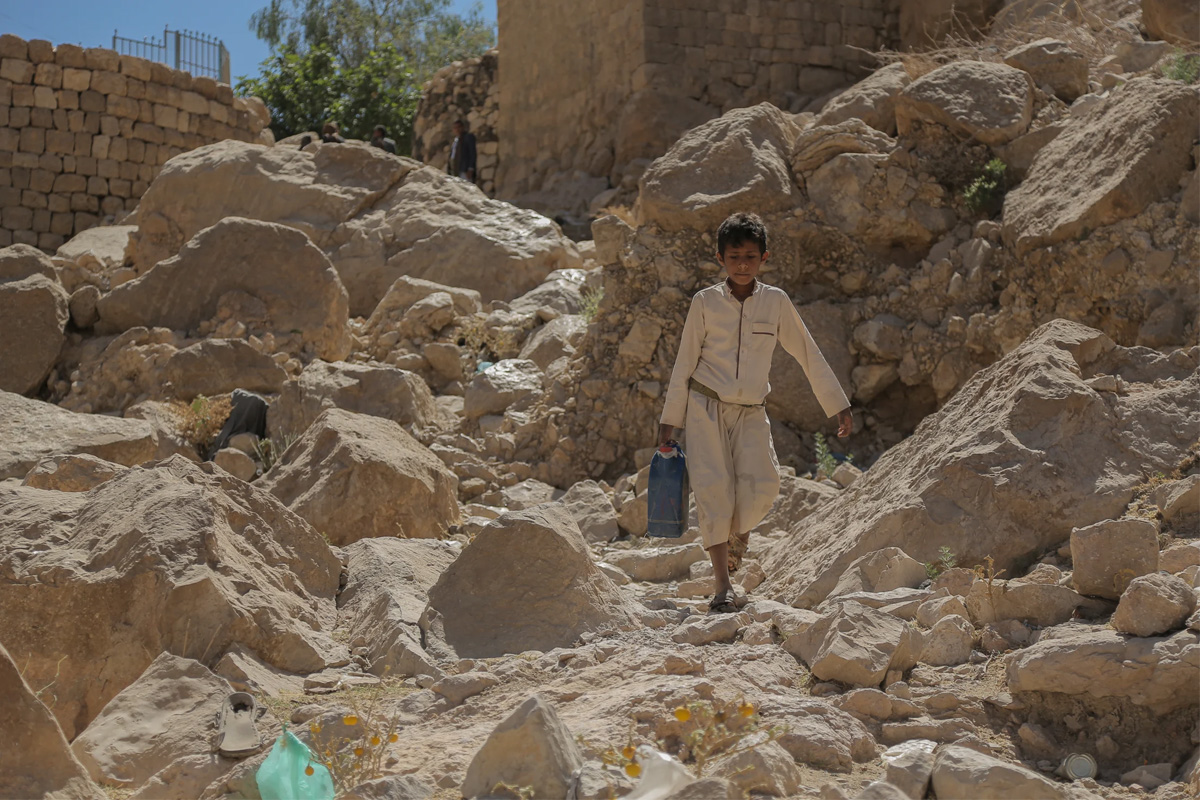 Boy carries a water jug through rocky terrain