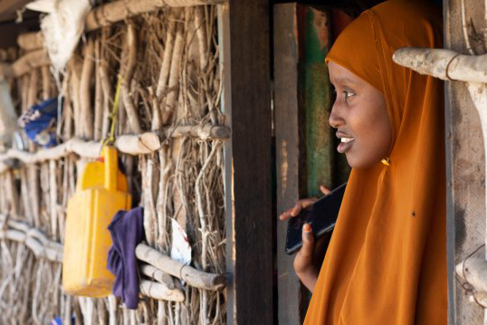 Quresho Abdirizak, a youth leader, stands outside her home holding her mobile phone. 