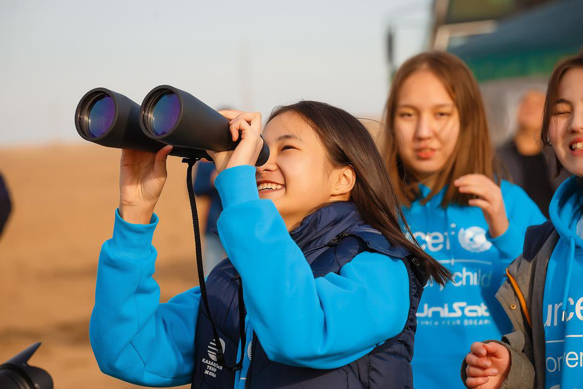 A girl looking into the sky with binoculars.
