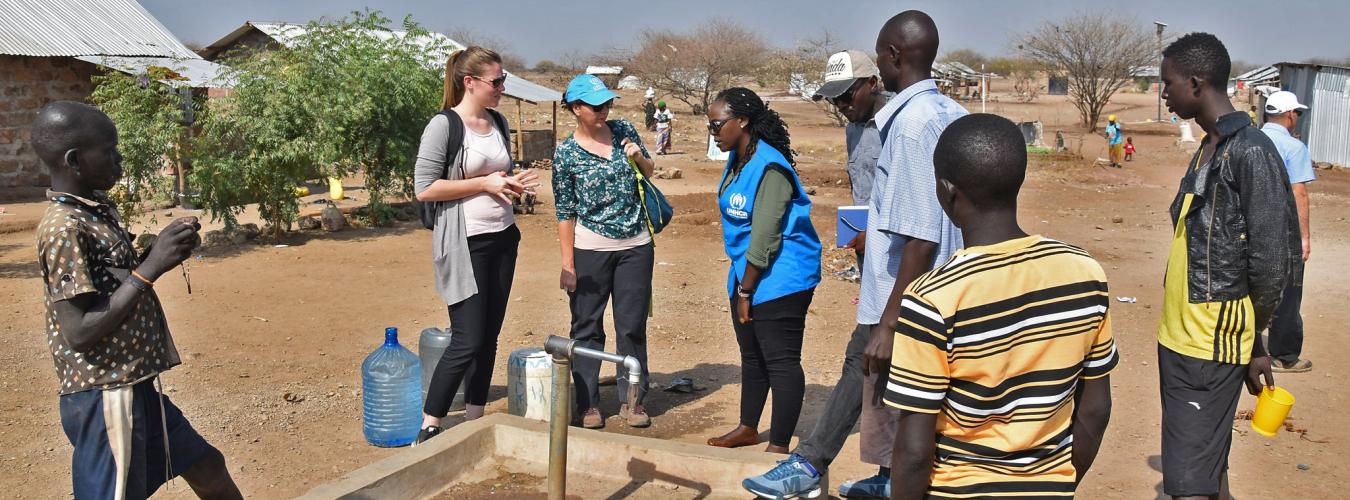 UNHCR staff member talks to a group about the solar powered water pump in the foreground.
