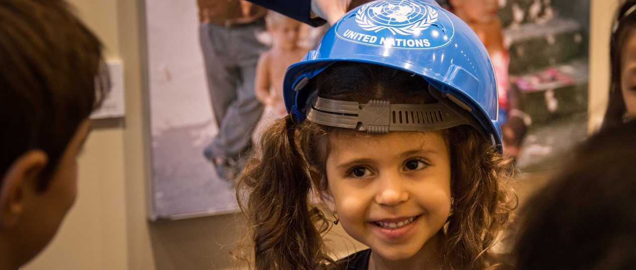 Young girl-child on UN Kids Tour wears a UN blue helmet