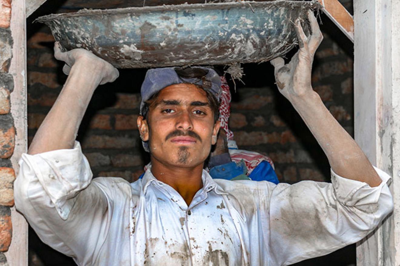 Un homme tient un grand bol sur sa tête avec un matériau de construction (comme de la boue).