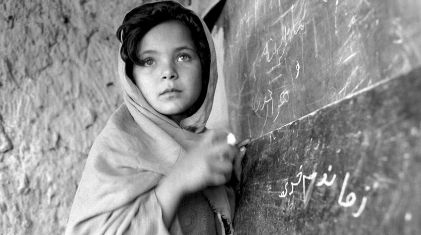 A young Afghan girl writes on chalkboard