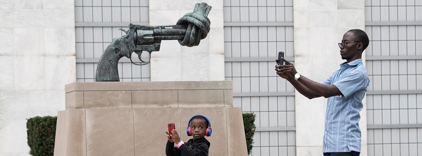 A man and his son stand next to the sculpture of a gun with a knotted barrel taking pictures.