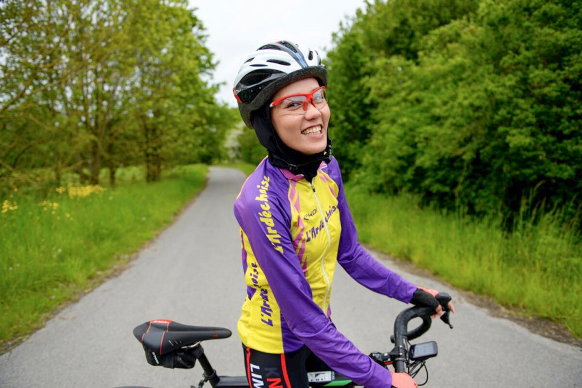 A woman in cycling gear with her bike smiles at the camera.
