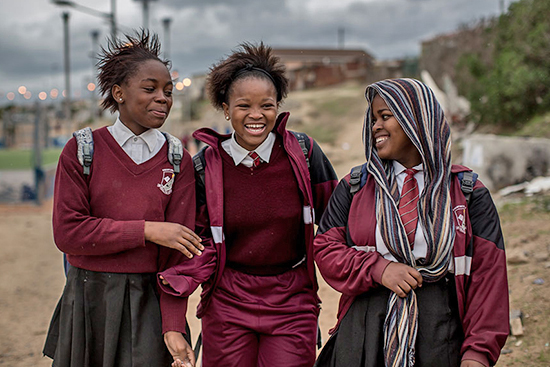 Three girls in primary school walking along road in Cape Town, South Africa.