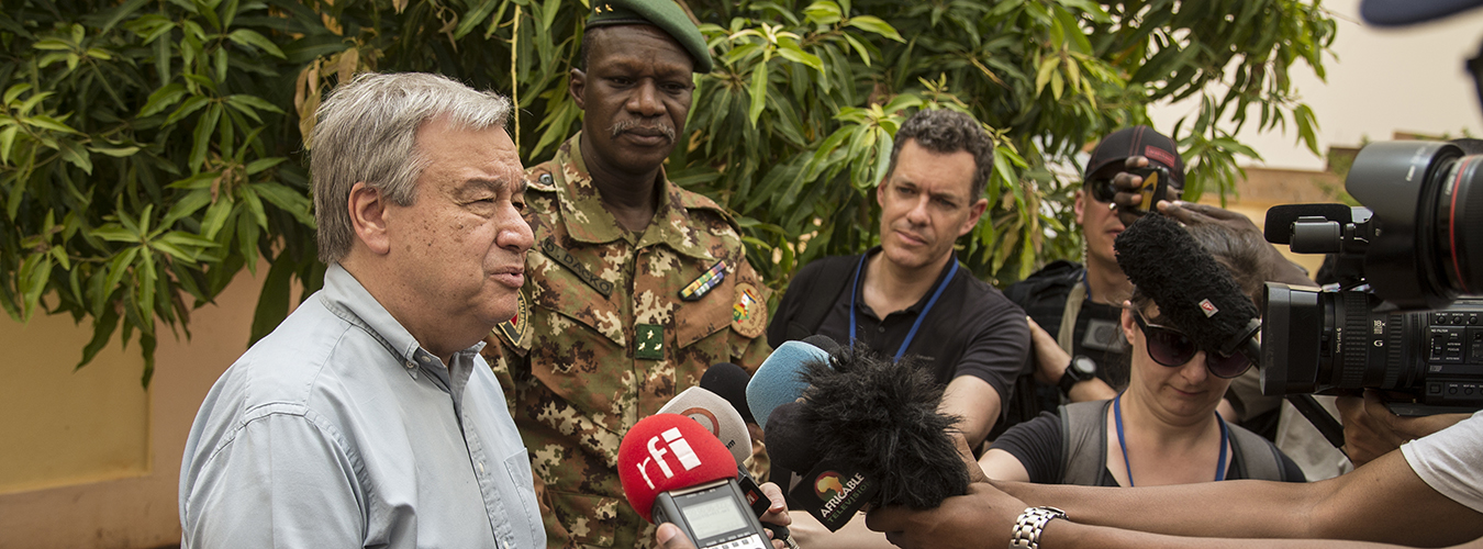 Secretary-General speaks into a microphone surrounded by men in military uniform and others.