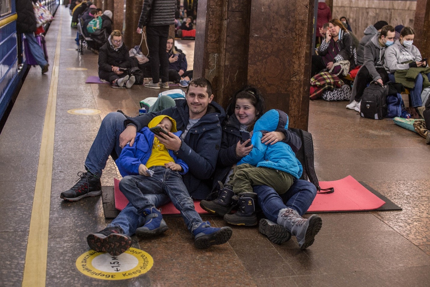 A family of four at a train station holding phones. 