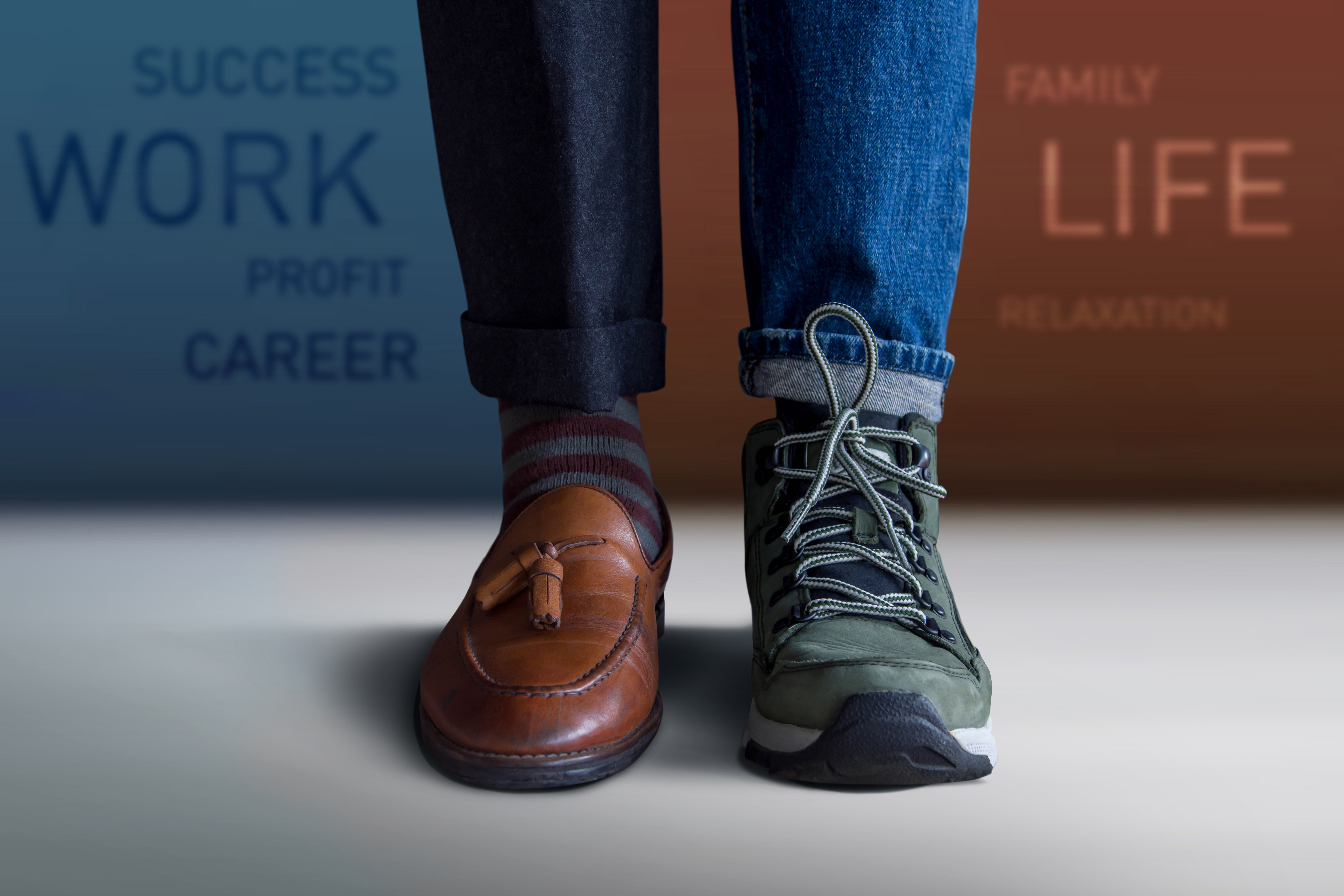 Close-up on a man’s feet: one with pants and dress shoe, the other with jeans and hiking boot. 