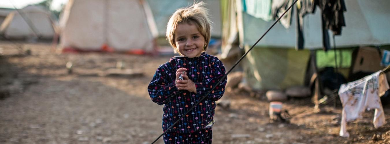 A young girl standing near tents in refugee camp in Iraq.